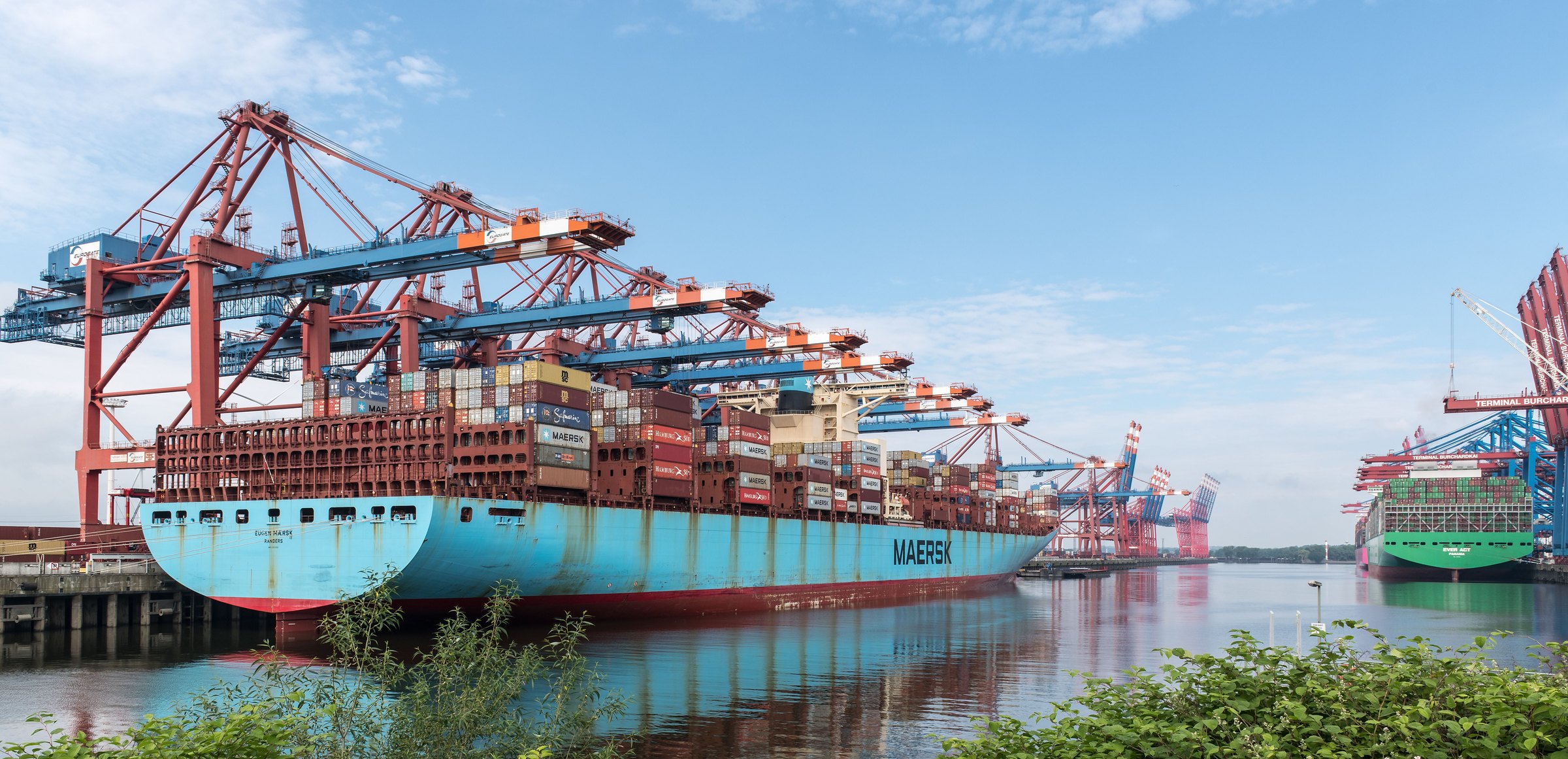 A container ship loading beneath gantry cranes at a port terminal